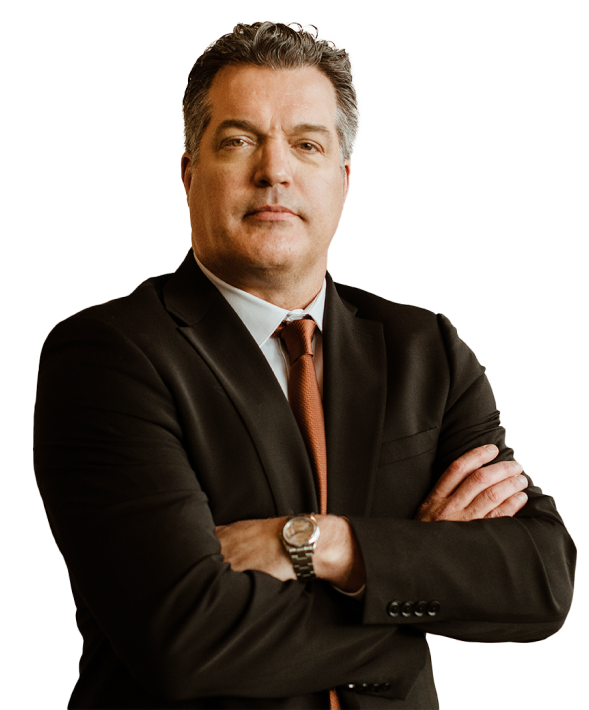 A man in a dark suit and tie stands with arms crossed, looking forward against a plain white background.