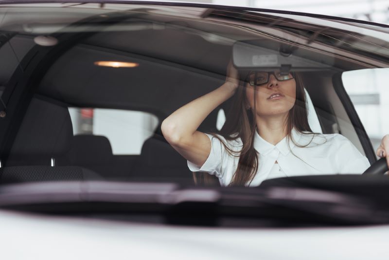 A woman adjusts the rearview mirror while sitting in the driver's seat of a car, looking at her reflection.