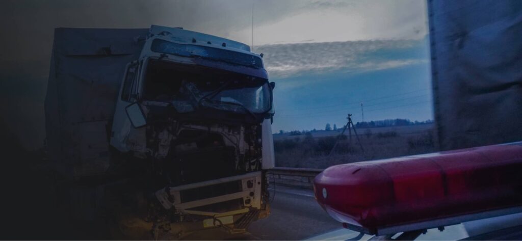 A damaged truck with a missing front hood is stopped on the side of a road near a police vehicle at dusk.