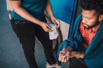 A person in a blue shirt prepares a medical test while another person sits nearby with their hand extended, appearing to await the procedure.